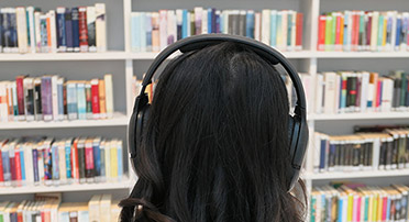 Eine Frau sitzt mit Kopfhörern vor einem Bücherregal